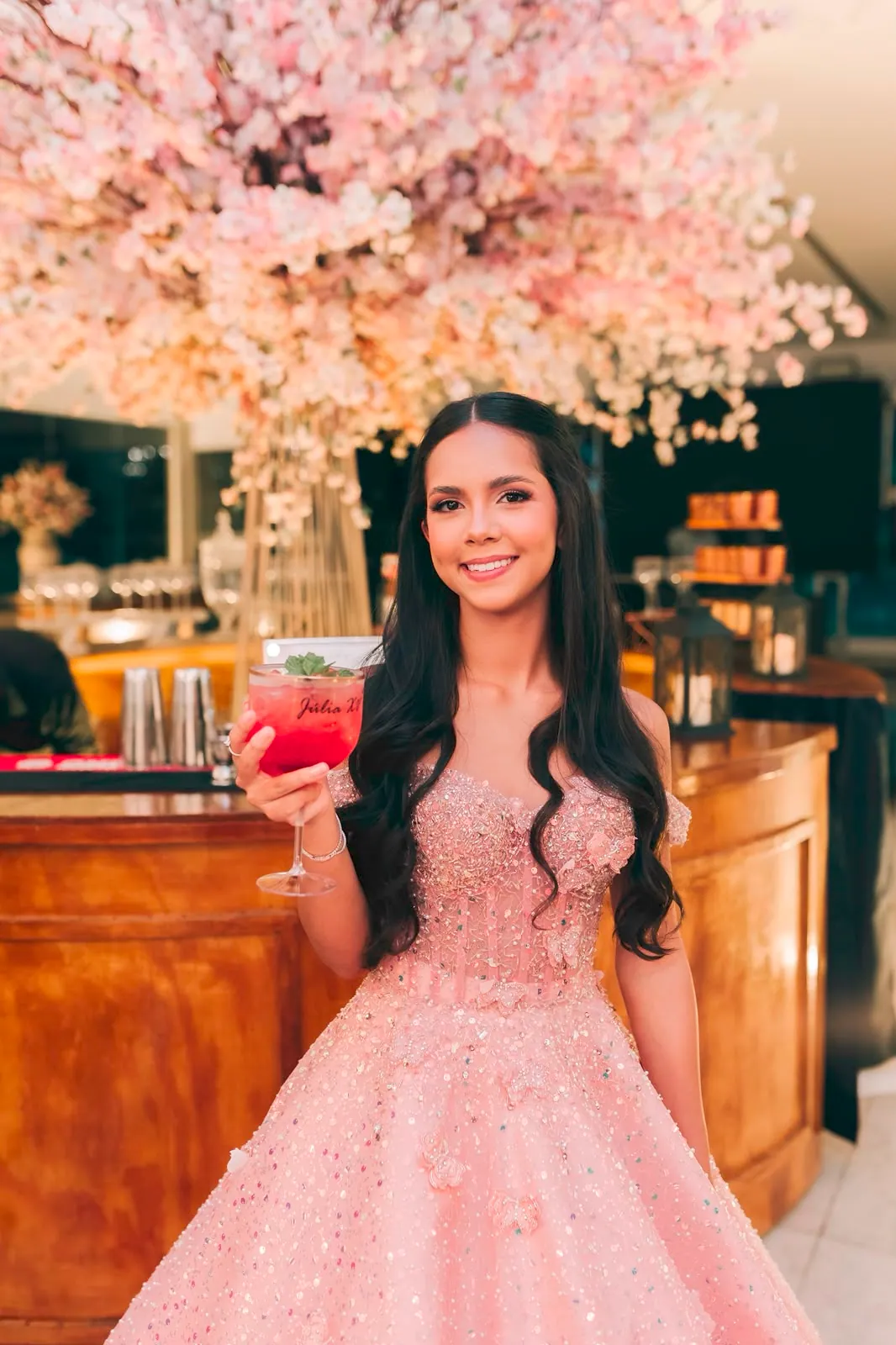 Debutante com drink personalizado sob árvore de cerejeira rosa na festa de 15 anos
